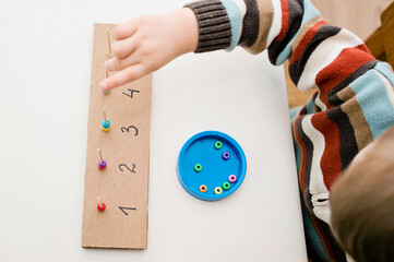 Home made montessori metodic tool for early education, learning to count. 2 year old boy puts beads on wooden rods. Children, people, infancy and education concept. Formation and development of the ch