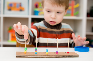 Home made montessori metodic tool for early education, learning to count. 2 year old boy puts beads on wooden rods. Children, people, infancy and education concept. Formation and development of the ch