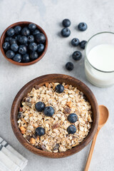 Oat muesli with blueberries in bowl and glass of milk on concrete background. Healthy breakfast food concept. Top view