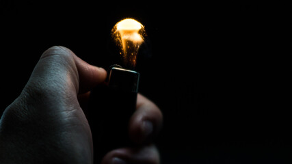 A person has lighters in his hands and he lights it through a flint wheel, the lighter ignites, sparks and fire appear, close-up on a black background.