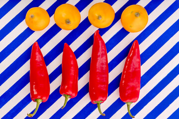Red sweet peppers and yellow tomatoes on a striped background.