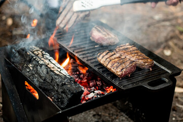 Beef steaks grilling on a cast iron plate on a camp fire. Campfire cooking. Outdoor BBQ. Selective focus.
