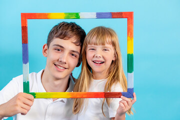 a 5-year-old girl and a teenage boy look at the camera through a colored frame and smile, on a blue background, copy space