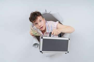 Pretty Woman is holding a suitcase full of money and emerging through torn paper hole in studio,...