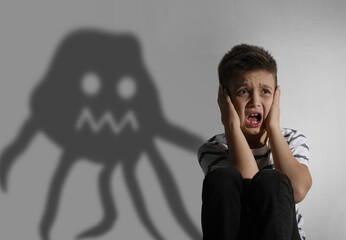 Scared little boy suffering from sciophobia and phantom behind him. Irrational fear of shadows