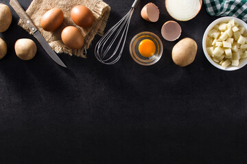 Spanish omelette tortilla ingredients: eggs, potatoes and onion on black slate background. Top view  copy space