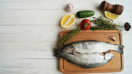 Two rainbow trout on a board, with herbs , ready for cooking.