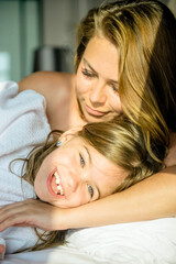 A mother hugs her daughter in bed. Her daughter looks at the camera and smiles. Mother and daughter sleep together. Cute girl with a gap between her baby teeth