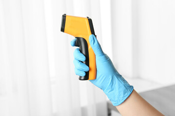 Doctor in gloves holding non contact infrared thermometer indoors, closeup