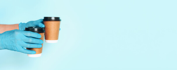 Coffee cup in hand with medical glove on blue background. Banner with copy space. Contactless delivery service during quarantine coronavirus pandemic. Take away only concept. Delivery service concept