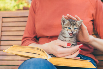 Cropped image of young woman sitting in the garden with book and tabby kitten making meow