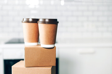 Craft paper cups with coffee to go and food box, lunch on tabletop over white kitchen. Banner, copy space. Safe delivery, take away only concept. Food delivery service during coronavirus pandemic