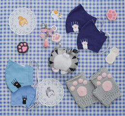 Cat lover items. Flat lay of cat lovers items including face mask, crochet gloves, coin purse, iron on patch and key chain on the blue gingham picnic cloth pattern.