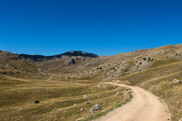 Old mountain road, rocky landscape, mountain top in the background with blue sky and moon. Bjelasnica Mountain, Bosnia and Herzegovina.