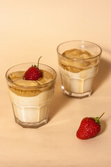 Dalgon coffee in a transparent glass with milk on a pastel background with strawberries. Vertical orientation