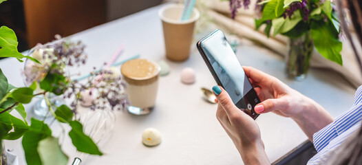 A woman is taking photos on a mobile phone camera of a whipped morning Dalgona coffee. White background, pastel colors and lilac flowers - Powered by Adobe