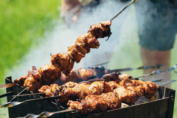 Guy, at summer party, cooking kebab on metal skewer. Roasted meat cooking process at barbecue. BBQ fresh pork meat chop slices. Grill on charcoal and flame, picnic, street food.