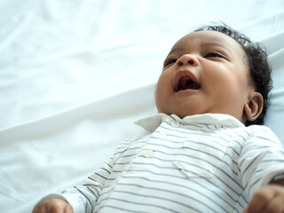 African baby boy is lying on the bed.