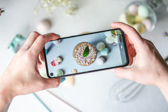 Woman is taking photos on a mobile phone camera of a whipped morning Dalgona coffee. White background, pastel colors and lilac flowers