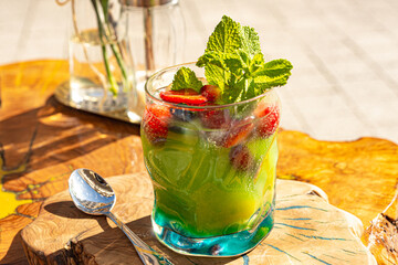 green ice tea with mint and strawberries in a glass