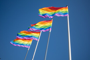 4 rainbow flags as a symbol for homosexuality hang next to each other and the sky is blue