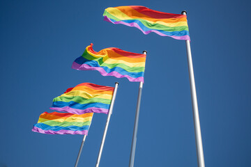4 rainbow flags as a symbol for homosexuality hang next to each other and the sky is blue