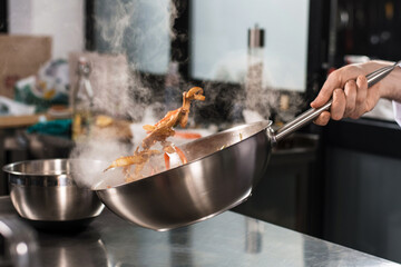 Chef hands toss food at kitchen. Closeup chef hands with wok cook food.