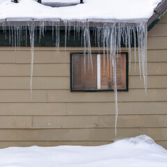 Square Snow covered roof with row of icicles over windows and wooden wall in Park City