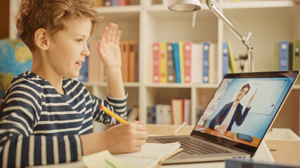 Fototapeta na wymiar Smart Little Boy Uses Laptop for Video Call with His Teacher. Screen Shows Online Lecture with Teacher Welcomes the Student with Waving Gesture, Boy Answers with Same. E-Education Distance Learning