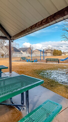 Vertical frame Green metal tables and benches inside a pavilion with melted snow on a sunny day