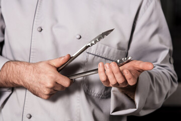 Chef prepare bbq at kitchen. Closeup male hands with metal tong.