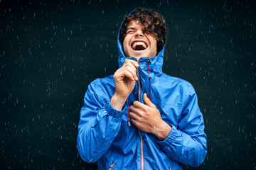 Happy man smiling broadly, wearing blue raincoat during the rain outside. Handsome male in blue...