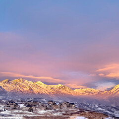 Fototapeta na wymiar Square frame Homes on snowy hill against frosted Wasatch Mountain with golden glow at sunset
