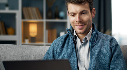 Smiling European man using digital gadget sitting on couch at home, cropped portrait