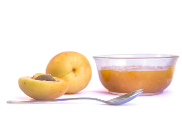 Naklejka na ściany i meble Ripe sweet apricots, glass bowl with homemade jam or marmalade and tea spoon on white background. Food ingredient. Fruits and vegetables. Homemade recipe.