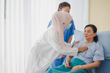 Young Asian woman Muslim doctor and nurse giving advice discussion and check up to elderly patient sitting in bed at hospital which smiling and felling happy. Medicine and health care safe concept.