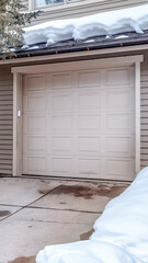 Vertical crop White garage door entrance of home with snow covered roof and yard in winter