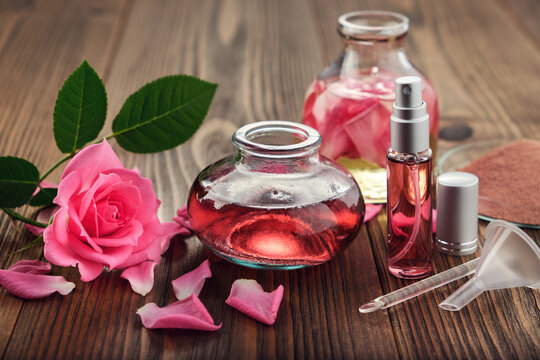 Rose flower, infused water and essential oil or rose blend bottle, flavored water in a spray bottle, pink clay powder, glass spatula and small funnel for making of cosmetic products at home.