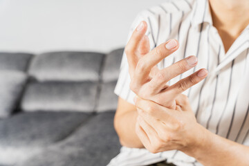 Young man suffering from hand pain while sitting on sofa at home. Healthcare medical or daily life concept.