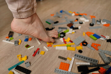 Fototapeta premium Foot stepping on plastic construction toys. Scattered toys on the floor. Gets severe pain.