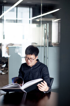 Asian Businessman Wearing Glasses Reading Book In Public Library. Education Research And Self Improvement With Printed Media. World Book Day Concept