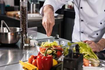 Chef man cook vegetables at kitchen restaurant. Closeup chef hand salted food.