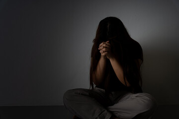 sad woman hug her knee and cry sitting alone in a dark room. Depression, unhappy, stressed and...