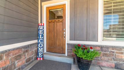 Panorama frame Brown front door with glass pane and Welcome sign against gray and stone wall