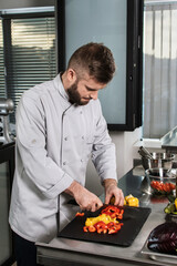 Chef man at kitchen with knife. Male professional cutting red and yellow pepper.