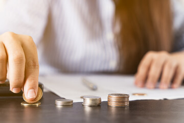 Close up coins on the desk with businesswoman working on desk office and holding a coin. Expenses, taxes, home budget finance accounting concept.