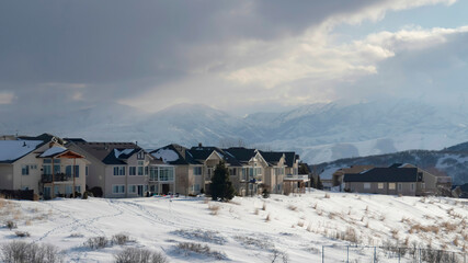 Panorama crop Homes on snowy terrain ovelooking Wasatch Mountain peak and dark overcast sky