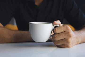 closeup hand of a businessman holding a white cup of coffee in the room with soft-focus and over light in the background