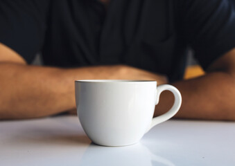 closeup hand of a businessman holding a white cup of coffee in the room with soft-focus and over light in the background