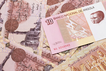 An red and white ten Angolan kwanza bank note on a background of Egyptian one pound bank notes